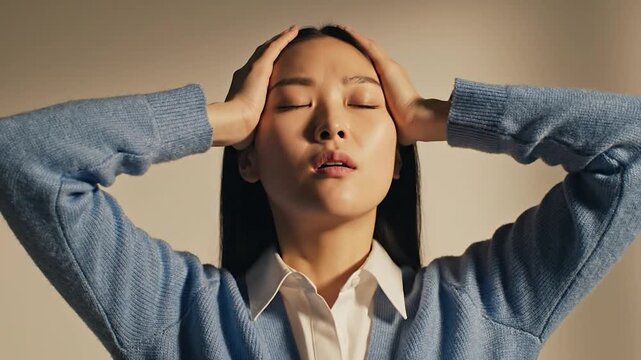 A woman with her hands on her temples and eyes closed in a stressful expression on a beige background