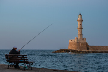 Pêcheur local assis sur un banc devant le phare vénitien de La Canée, Crète, Grèce, au coucher ou au lever du soleil © Etienne