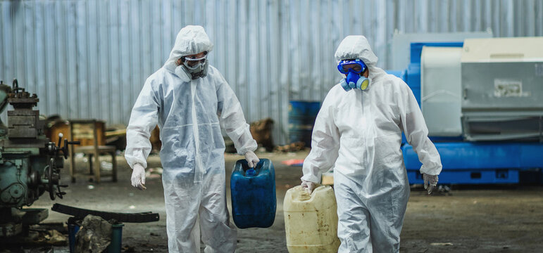 Two people in hazmat suits are carrying blue and white containers