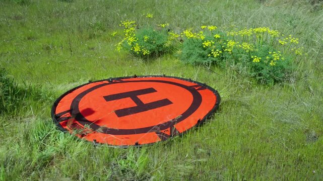 A First Person View (FPV) drone with a mounted GoPro action camera landing on an orange hoodman helipad as the wind blows through green grass and yellow flowers