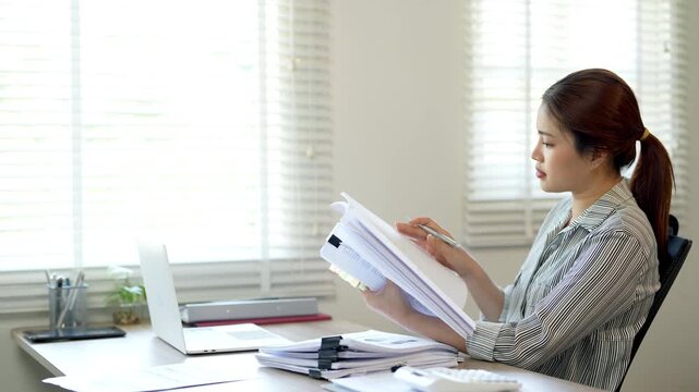 Focused young asian woman looking through paper documents, managing business affairs, summarizing taxes, planning future investments, accounting alone at home office. 