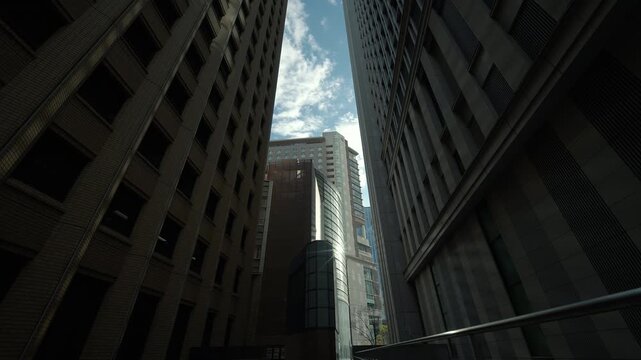 Narrow street view looking up at curved modern architecture in central Tokyo.