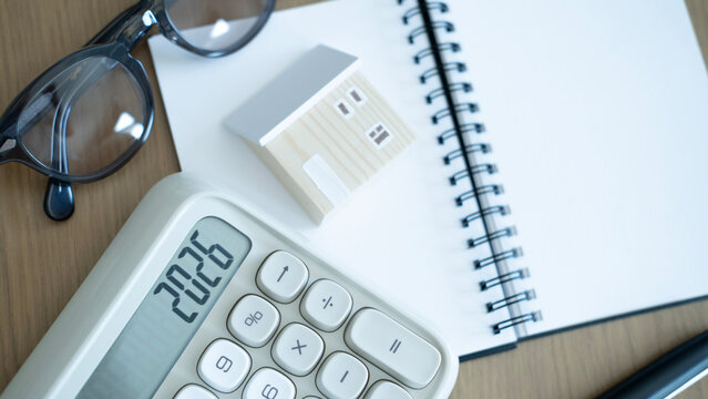 Calculator, notebook and small house model on wooden desk, concept of home insurance planning, mortgage calculation and personal financial protection.
