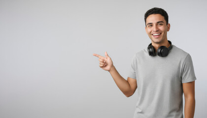 A hispanic male student with tan skin, wearing headphones and a casual gray t-shirt, smiling while pointing to his left side. Image embodies a youthful and tech-savvy lifestyle