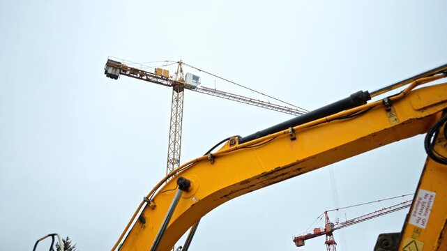 Close up of hydraulic machinery with a tall crane in the background. Industrial building site with heavy equipment under a cloudy sky. Professional civil engineering project.