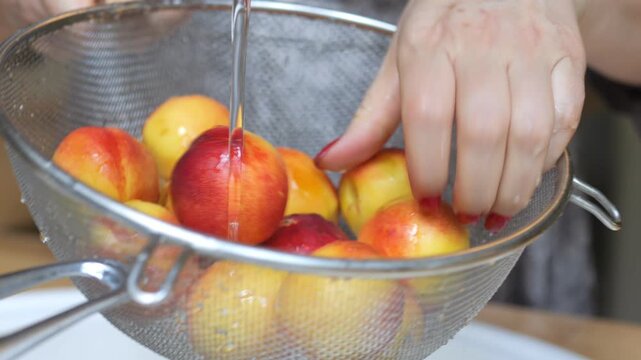 Woman is washing apples in a colander. The apples are in a bowl and the colander is in a sink