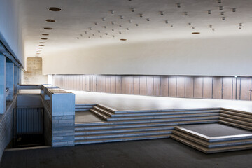Obraz premium Abandoned city hall interior with modernist architecture featuring tiered concrete platforms and wood panelling. An empty municipal government building showing brutalist design with geometric steps