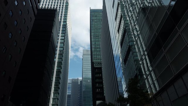 Towering gray skyscrapers looking up from a narrow urban alley in Tokyo's financial center.