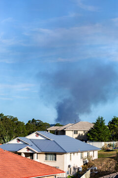 Black smoke billowing into sky behind residential buildings from bushfire near town