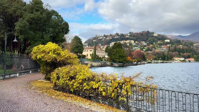 Beautiful view of Como lake, Italy. Promenade with green trees in Como town. Clouds over the Alps mountains. Beautiful landscape at sunny day
