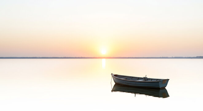 Barque solitaire immobile sur l'eau paisible au lever du soleil lumi�re douce et reflets dor�s sur un calme absolu. AI Generated
