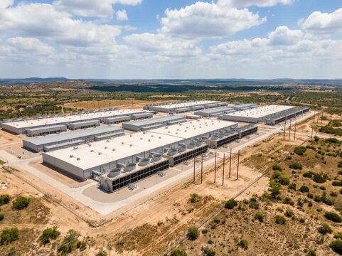 An aerial view of a large hyperscale data center in Texas, featuring expansive low-rise server buildings surrounded by dry landscape and open skies.