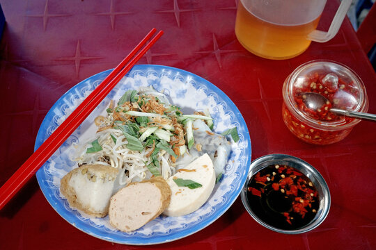 authentic vietnamese steamed rice rolls banh cuon dish with pork sausage and herbs. street food breakfast plate served with spicy dipping sauce on red plastic table.