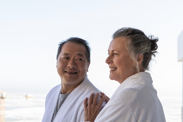 Obraz premium Senior couple standing on balcony overlooking calm sea wearing bathrobes near metal railing