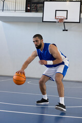 Fototapeta premium Adult male basketball player dribbling orange ball in gear on court under hoop, railing