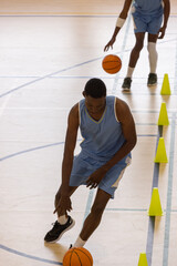 Fototapeta premium African american male teammates dribbling orange basketballs between yellow cones on court