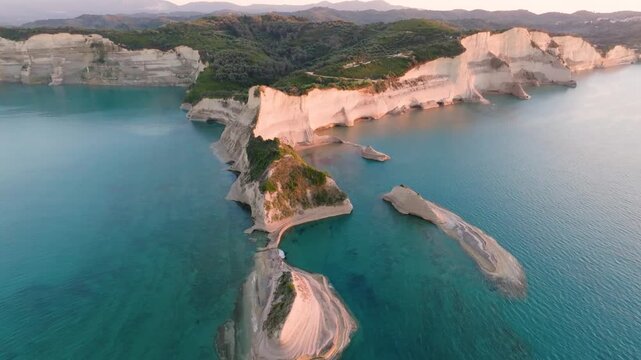Aerial drone footage flying over the unique geological formations and white cliffs of Cape Drastis, Corfu, Greece, highlighted by the warm light of sunset