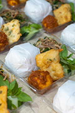 Close up of Indonesian traditional rice meal with paper wrapped rice, urap vegetables, balado egg and tempe mendoan. Popular street food and takeaway cuisine from Indonesia