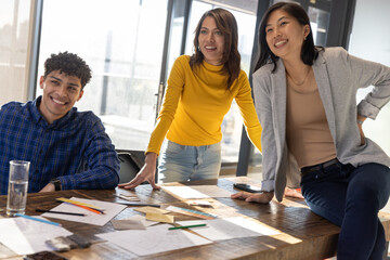 Diverse coworkers leaning on table collaborating on design in office with sketches and swatches
