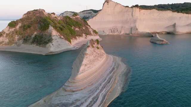 Aerial drone footage flying low over a long, narrow sea stack at Cape Drastis, Corfu, Greece. Cinematic reveal of the stunning white cliffs and turquoise water