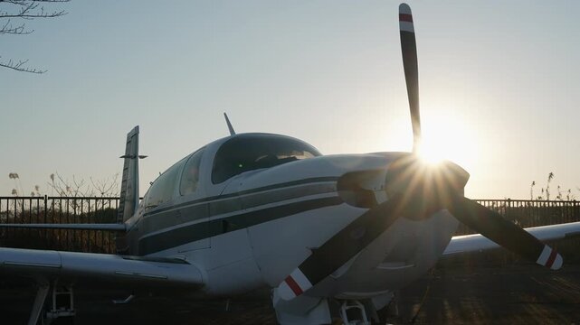 Private propeller plane parked on an airfield runway at sunset.