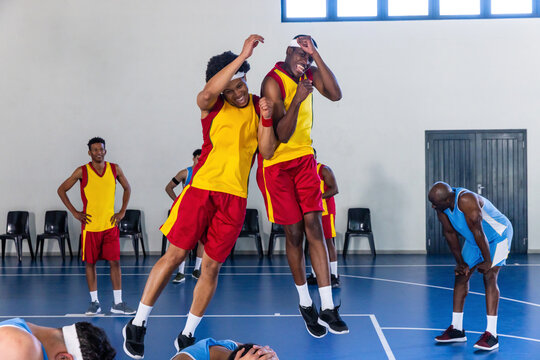 African american male basketball players jumping locking hands on court in yellow red jerseys