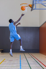 Obraz premium Male basketball player performing layup toward hoop inside gymnasium on court with lines