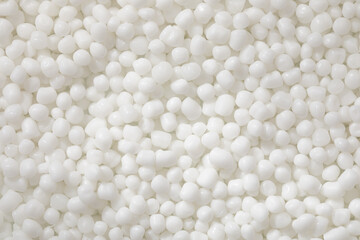 A top-down macro photo shows a dense, uniform collection of polymer granules, bright white and with...