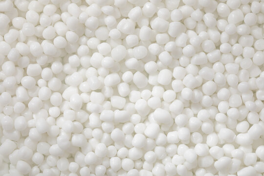 A top-down macro photo shows a dense, uniform collection of polymer granules, bright white and with a smooth matte finish.