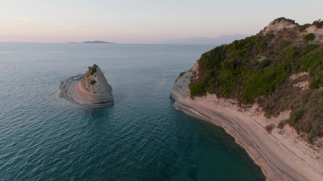Aerial pan shot revealing a secluded sea stack next to the massive white cliffs of Cape Drastis, Corfu, Greece, during a calm evening at sunset