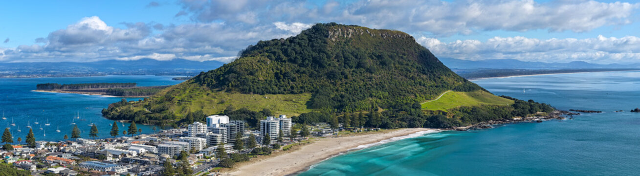 Aerial view of the iconic Mount Maunganui, its lush green slopes contrasting sharply with the turquoise ocean and sandy beach, Mount Maunganui, Bay of Plenty Region, New Zealand.