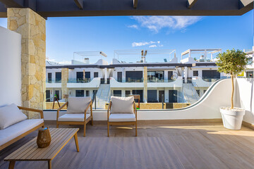 Naklejka premium Sunny modern apartment balcony with wood furniture and view of white minimalist buildings