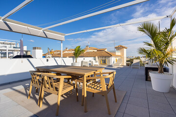 Modern rooftop patio with wooden dining set and pergola overlooking tiled rooftops
