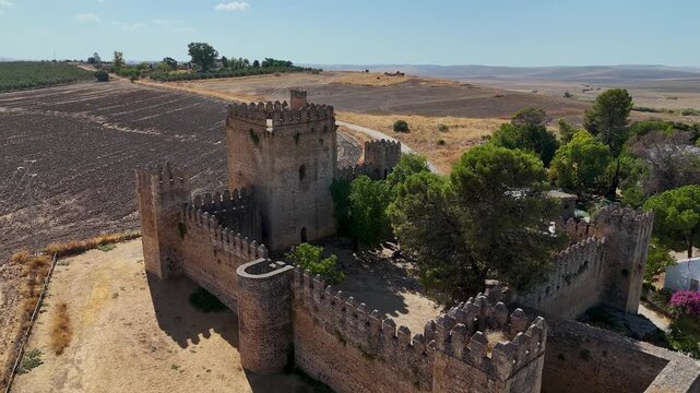 NEED YOUR ATENTION - An aerial Orbit Shot circles an ancient stone fortress ruin, showing its towers and walls set against a dry rural landscape under a sunny sky.