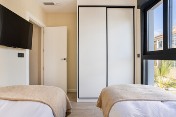 Bright twin bedroom with sliding wardrobe, large window and neutral tones in modern apartment