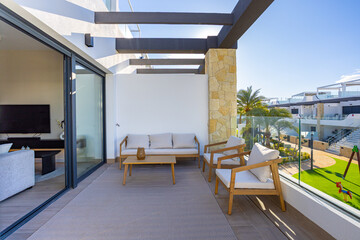 Modern apartment balcony with outdoor seating and garden view in sunny daylight setting