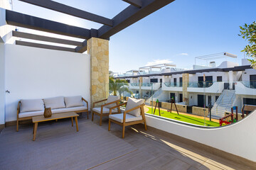 Sunny apartment balcony with lounge furniture and playground view in modern residential complex