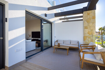 Sunny apartment terrace with outdoor lounge furniture and modern glass sliding doors