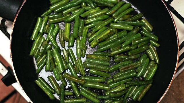 Close-up view of fresh green beans being pan-fried in a black skillet on a stovetop