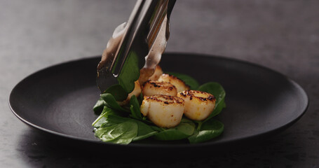 put roasted scallops on spinach in black plate