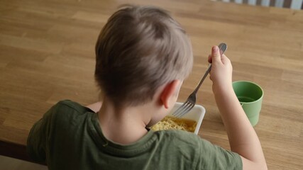 6 years old boy eats instant noodle from box. Child is eating Asian ramen. Lunch time. A good appetite. Tasty children food. Close-up portrait. Carbs dinner. Fast food. Kid eating by himself with fork
