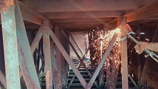 Worker welding metal beams on rusty bridge structure