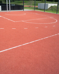 Basketball court surface with red flooring near sports facility during daytime hours