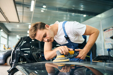 Caucasian man using car polishing machine in repair mechanic painting shop