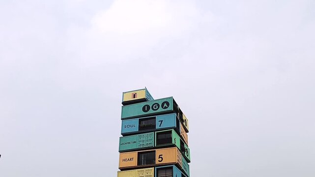 Vibrant stacked shipping containers against cloudy sky.The image displays the distinctive, stacked-container office of Ishwar Gehi Architects (IGA) in Surat, Gujarat. 