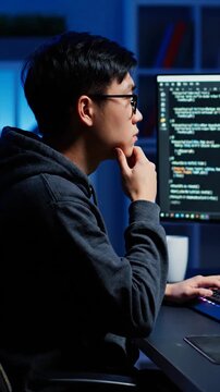 Asian Man Coding in Dim Blue Lit Room with Computer Screen. Software Developer in Contemplative Mood at Night. Cinematic Portrait of Programmer at Work.