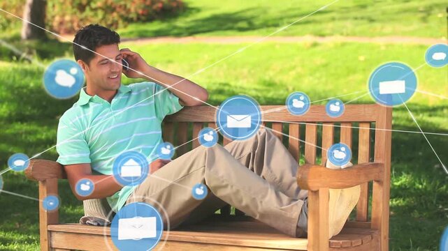 Animation of digital icons over caucasian man talking on smartphone sitting on the bench in tha park