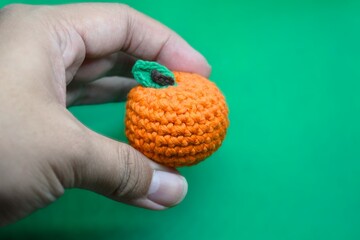 Handmade Amigurumi Orange Fruit Crochet Toy Held in Palm on Green Background