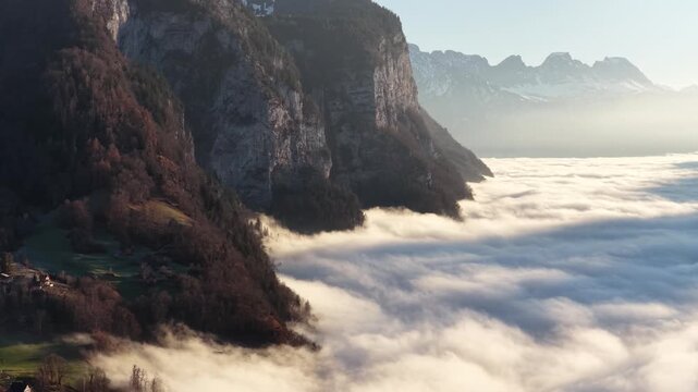 Churfirsten mountains Switzerland with steep rocky cliffs rising above thick cloud inversion as drone view of alpine valley and calm morning atmosphere.