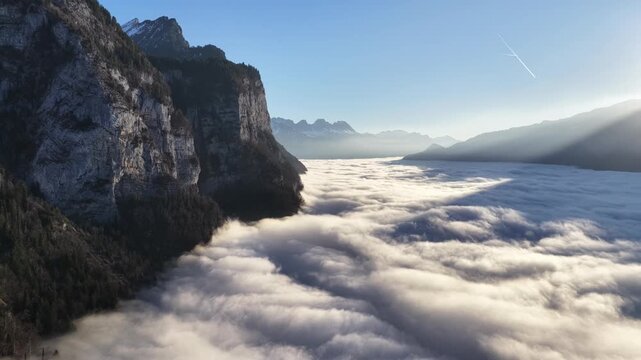 Churfirsten alps Switzerland massive cliffs above rolling cloud sea as drone pulls back over wide alpine valley and peaceful morning landscape.